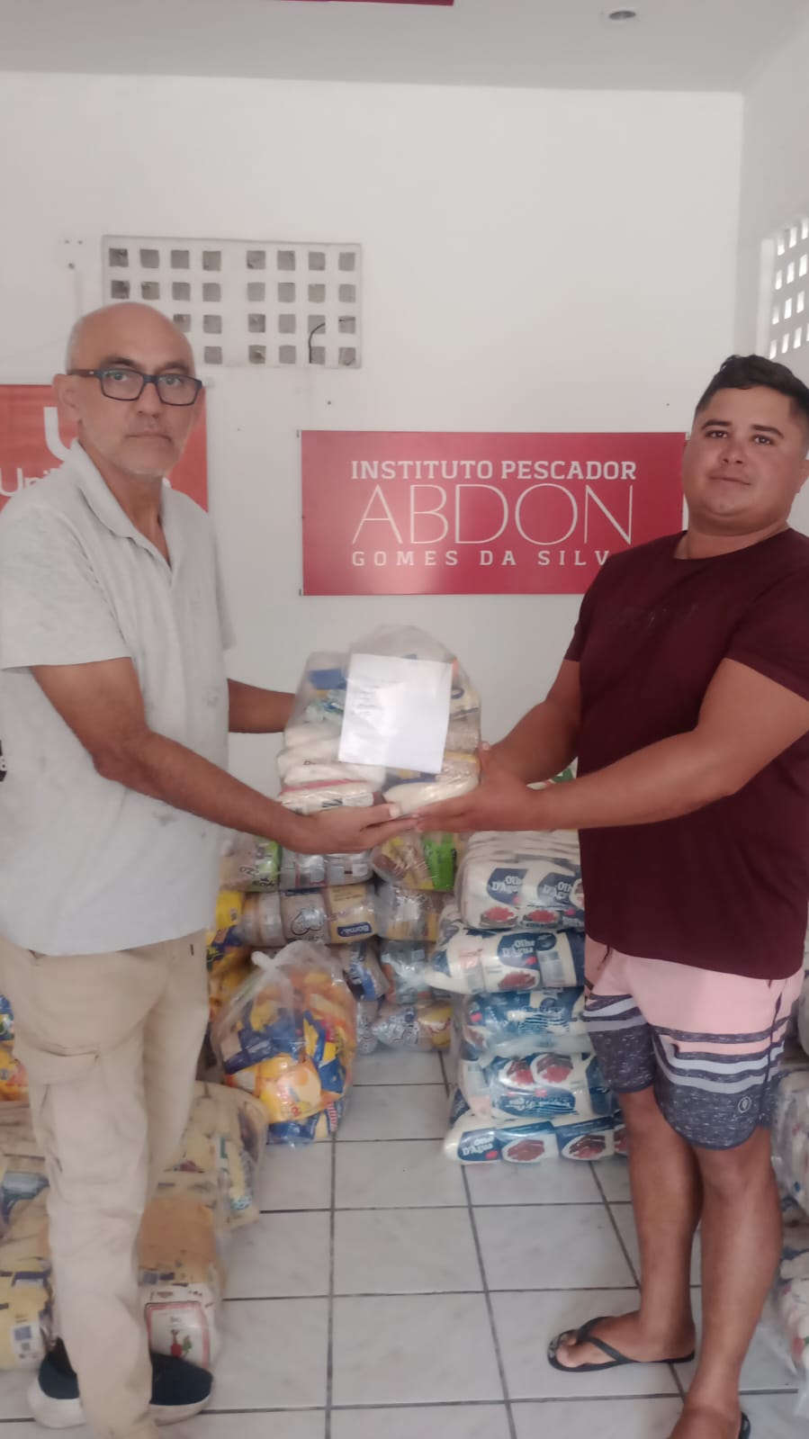 Represente do Instituto Pescador Abdon Gomes da Silva entregando cesta básica a um membro da comunidade durante a distribuição de cestas básicas.